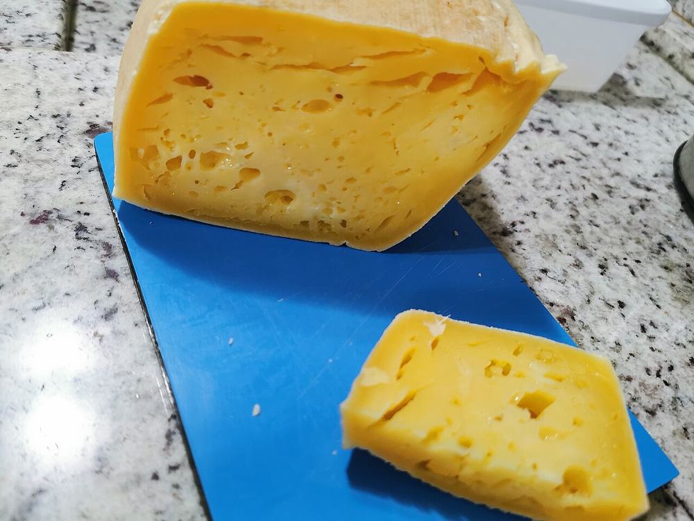 Queijo colonial cortado, com a massa amarela e furada à mostra